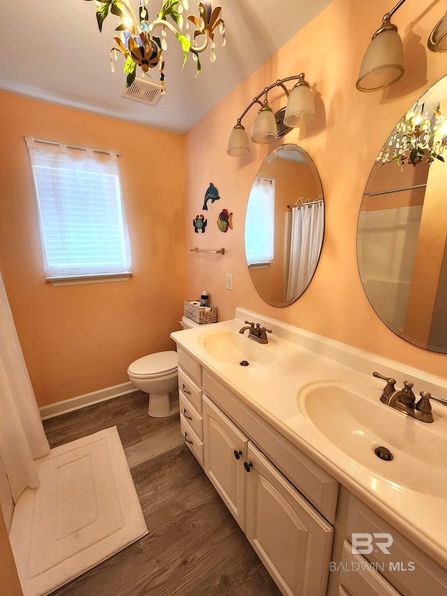 bathroom with wood-type flooring, toilet, vanity, and a chandelier