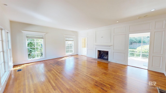 unfurnished living room with a fireplace with flush hearth, wood finished floors, visible vents, and a healthy amount of sunlight