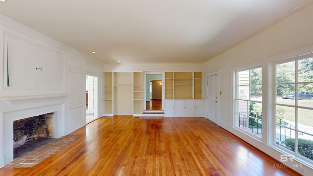 unfurnished living room featuring built in shelves, a wealth of natural light, a fireplace with flush hearth, and light wood finished floors