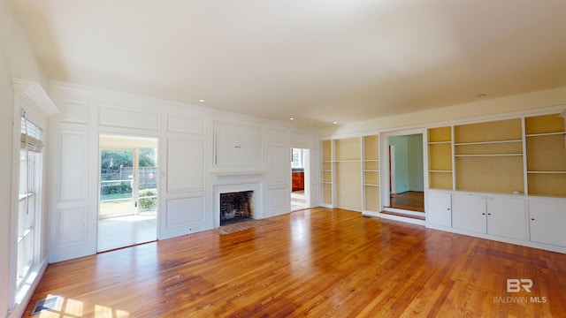 unfurnished living room with a decorative wall, a fireplace with flush hearth, wood finished floors, and visible vents