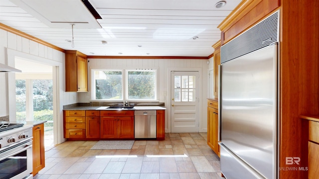 kitchen with wooden walls, a sink, appliances with stainless steel finishes, crown molding, and brown cabinets