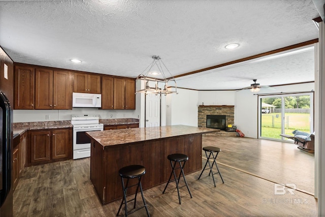 19300 Community Ln, Summerdale, AL 36580 - kitchen with white appliances, a textured ceiling, dark wood-type flooring, a kitchen island, and a stone fireplace