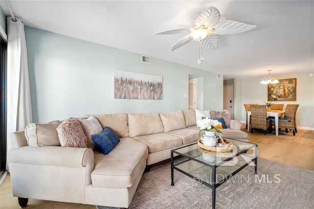 living room featuring ceiling fan with notable chandelier, visible vents, and light wood-style floors