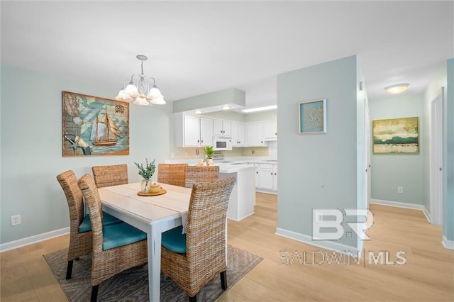 dining area featuring a chandelier, light wood-style floors, and baseboards