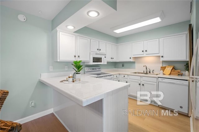 kitchen featuring a peninsula, white appliances, a sink, white cabinetry, and baseboards