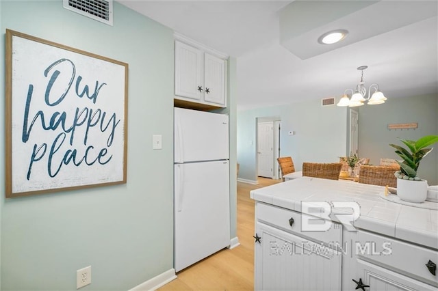 kitchen with visible vents, tile counters, freestanding refrigerator, and white cabinetry