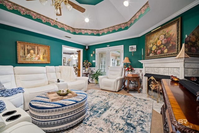 living room featuring a raised ceiling, a fireplace, ceiling fan, and crown molding