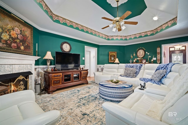 living room featuring a fireplace, ceiling fan, a tray ceiling, and crown molding