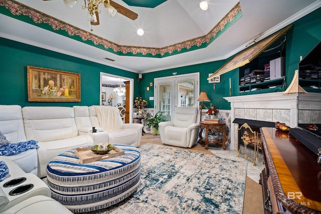 living room featuring a raised ceiling, french doors, crown molding, a tiled fireplace, and ceiling fan