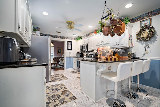 kitchen featuring appliances with stainless steel finishes, kitchen peninsula, ceiling fan, decorative backsplash, and white cabinetry