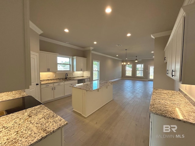 kitchen with white cabinetry, a kitchen island, light stone countertops, and pendant lighting