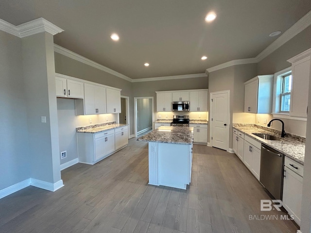 kitchen featuring appliances with stainless steel finishes, sink, stone countertops, a center island, and white cabinetry