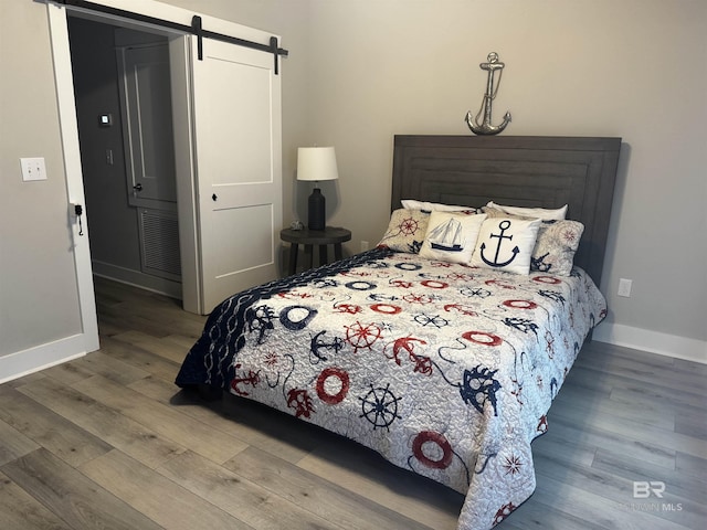 bedroom with a barn door, visible vents, baseboards, and wood finished floors