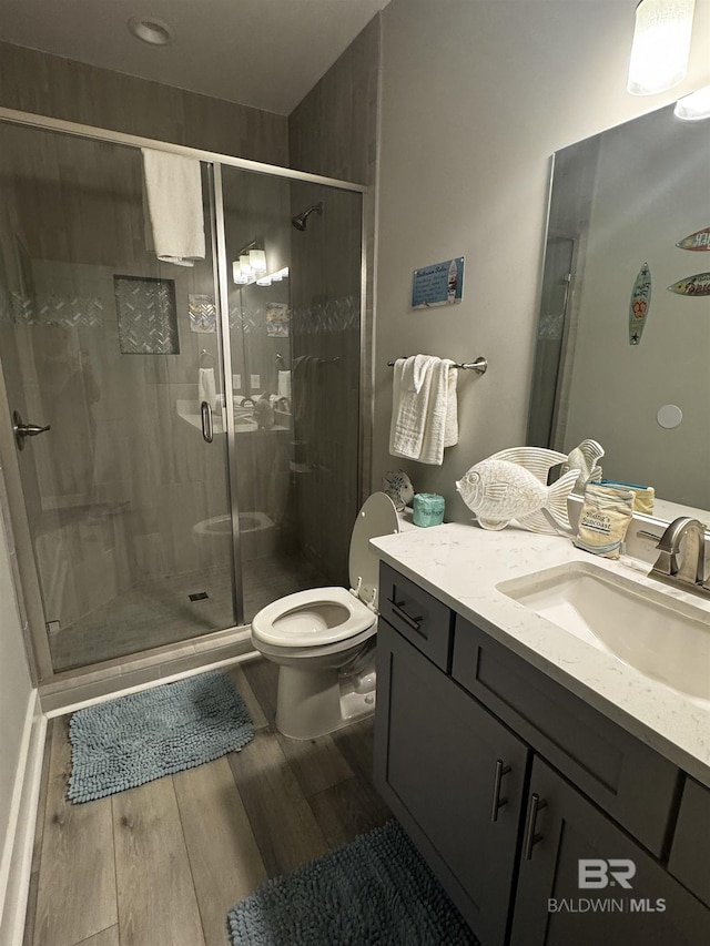 bathroom with toilet, a stall shower, wood finished floors, and vanity