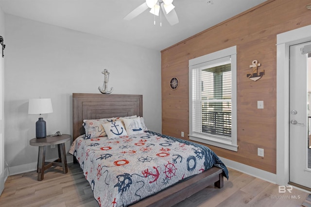 bedroom featuring wood walls, baseboards, ceiling fan, and wood finished floors
