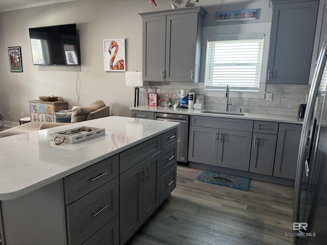 kitchen with gray cabinets, backsplash, appliances with stainless steel finishes, a sink, and wood finished floors