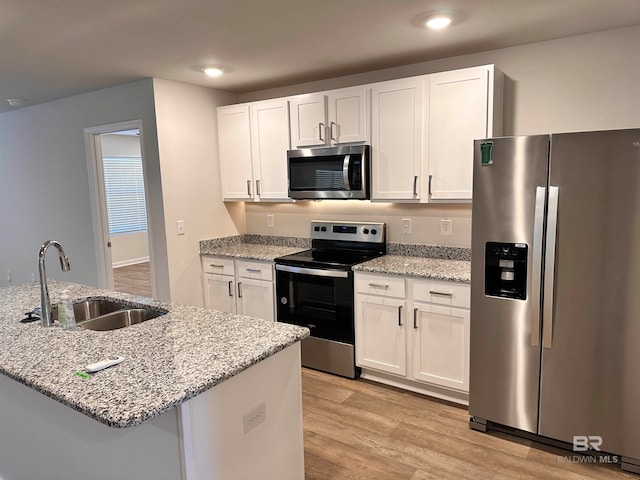 kitchen with sink, light hardwood / wood-style flooring, light stone countertops, appliances with stainless steel finishes, and white cabinetry