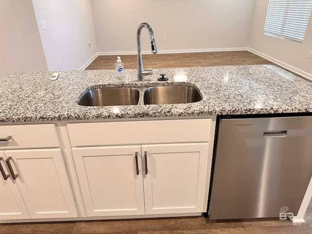 kitchen with dishwasher, white cabinets, sink, light stone countertops, and dark hardwood / wood-style flooring