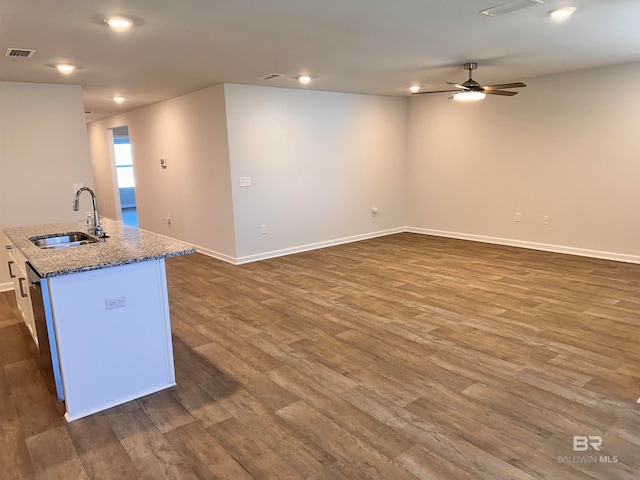 kitchen with a kitchen island with sink, sink, dark hardwood / wood-style floors, ceiling fan, and light stone countertops