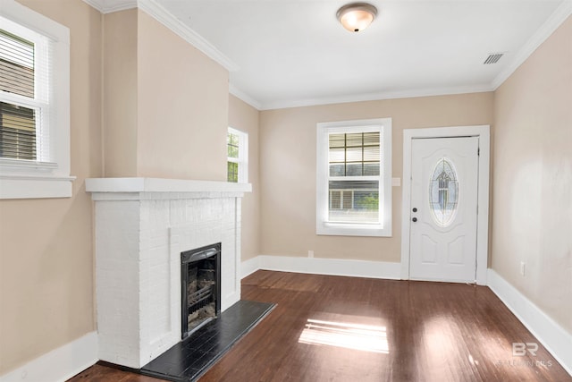 entrance foyer with dark wood finished floors, a brick fireplace, ornamental molding, and visible vents