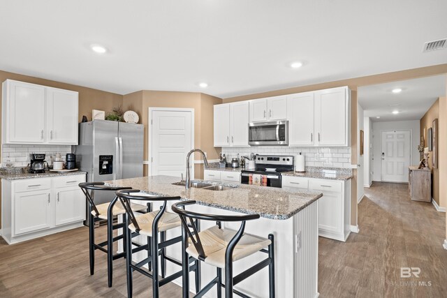 14705 Forsythia Loop, Silverhill, AL 36576 - kitchen featuring stainless steel appliances, decorative backsplash, a breakfast bar area, white cabinets, and light wood finished floors