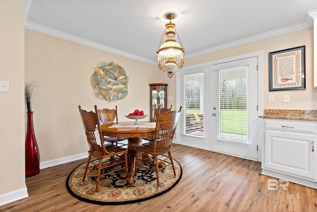 dining space featuring light wood finished floors, a chandelier, crown molding, and baseboards