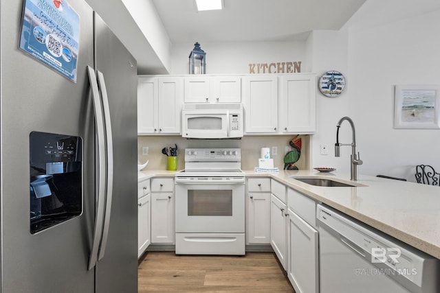 kitchen with light stone counters, white cabinetry, a sink, wood finished floors, and white appliances
