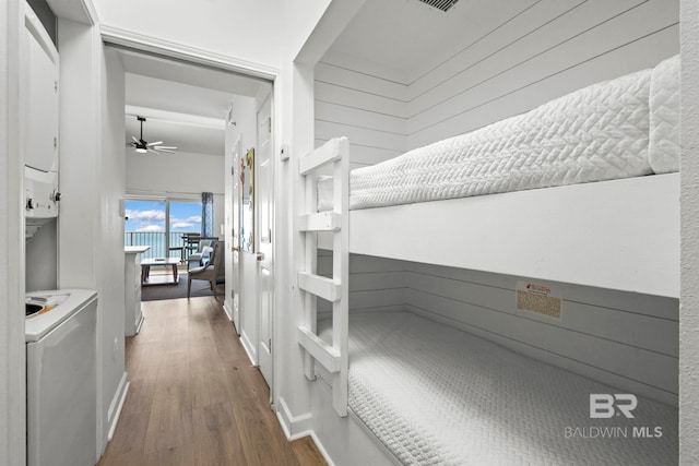 corridor with stacked washer / drying machine, visible vents, wood walls, and wood finished floors