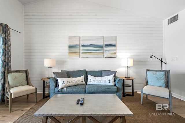 living area with lofted ceiling, baseboards, visible vents, and wood finished floors