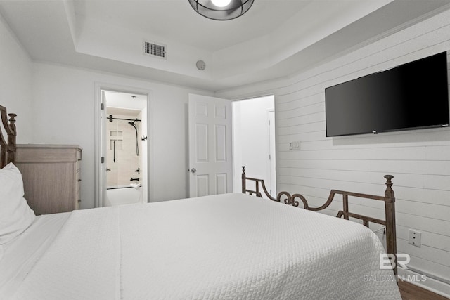 bedroom with wood walls, ensuite bath, visible vents, and a raised ceiling