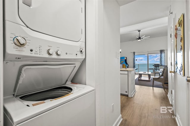clothes washing area featuring ceiling fan, stacked washing maching and dryer, baseboards, and light wood-style floors