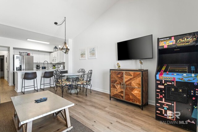 living room featuring high vaulted ceiling, a notable chandelier, light wood-style flooring, and baseboards