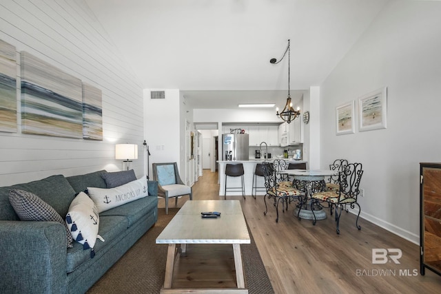 living area featuring visible vents, wood walls, a notable chandelier, and wood finished floors