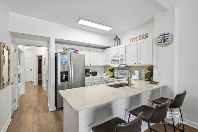 kitchen with a breakfast bar area, white cabinets, a sink, white appliances, and a peninsula