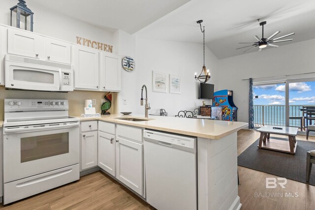 kitchen featuring white appliances, open floor plan, a peninsula, light countertops, and a sink
