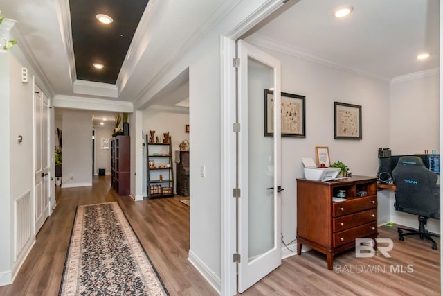 hallway featuring wood finished floors, crown molding, a desk, and baseboards