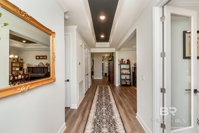 hallway with wood finished floors, a raised ceiling, ornamental molding, and baseboards