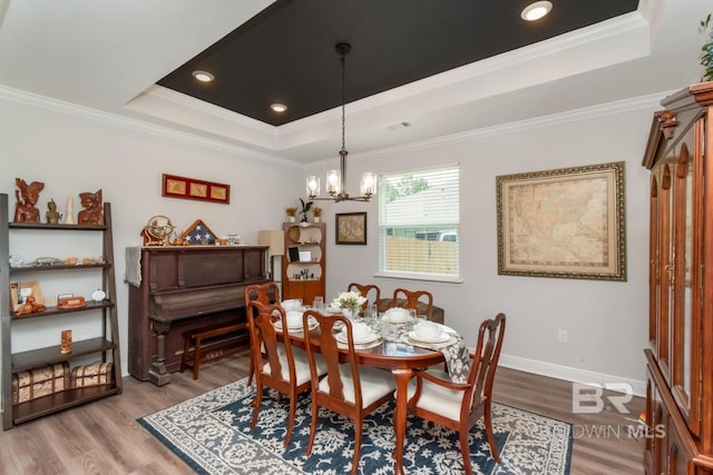 dining space featuring a raised ceiling, a chandelier, light wood finished floors, ornamental molding, and baseboards