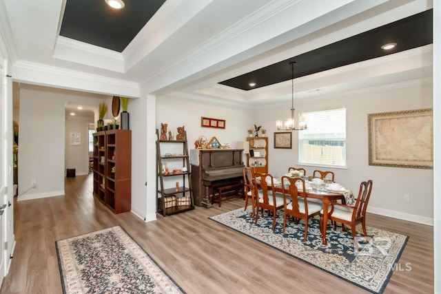 dining area with a tray ceiling, wood finished floors, crown molding, a chandelier, and baseboards