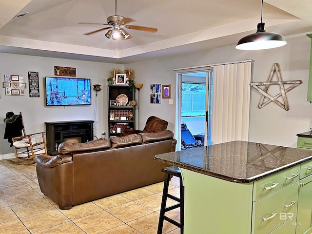 living area with light tile patterned floors, ceiling fan, a raised ceiling, and a fireplace