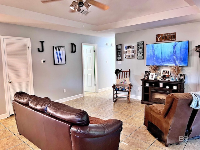 living area featuring light tile patterned flooring, ceiling fan, baseboards, and a tray ceiling