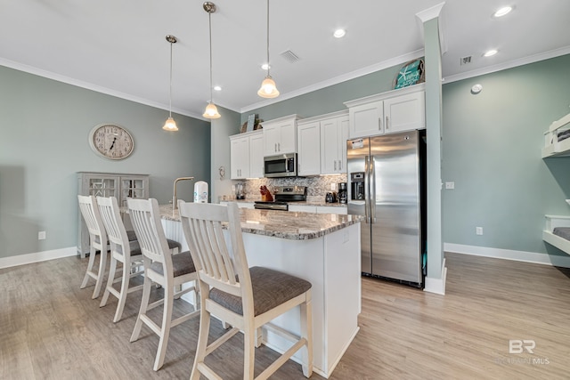 kitchen with a breakfast bar, pendant lighting, stainless steel appliances, visible vents, and white cabinets