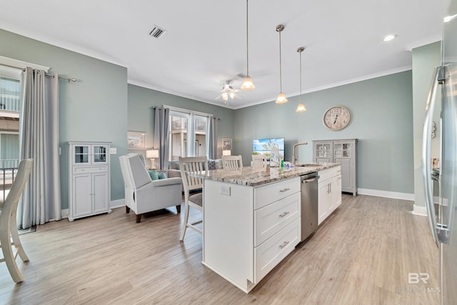 kitchen featuring light stone counters, pendant lighting, stainless steel appliances, white cabinets, and an island with sink