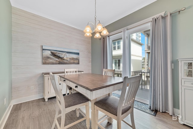 dining room with baseboards, light wood finished floors, wood walls, and a notable chandelier