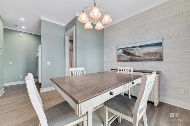 dining area with an inviting chandelier, an accent wall, ornamental molding, wood finished floors, and baseboards