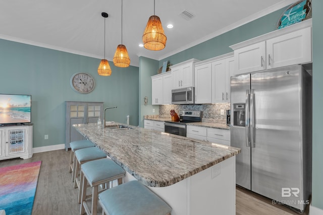 kitchen with appliances with stainless steel finishes, a sink, white cabinets, tasteful backsplash, and light wood-type flooring