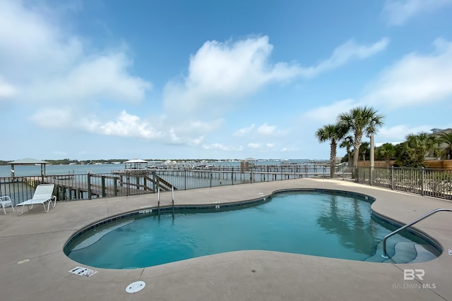 community pool with a patio area, a water view, and fence