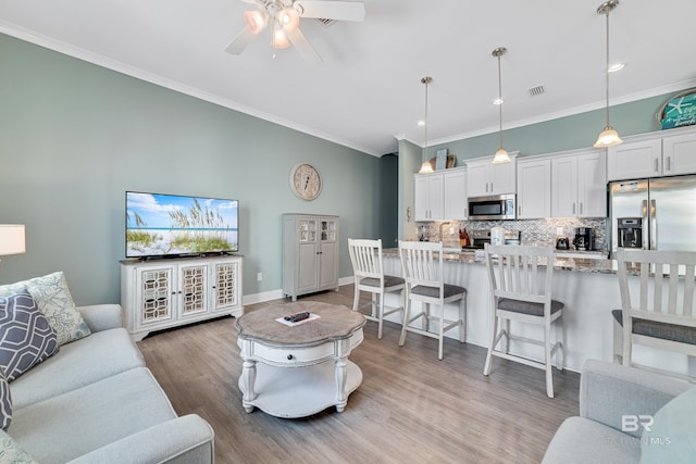 living room with light wood-style floors, visible vents, ornamental molding, and ceiling fan