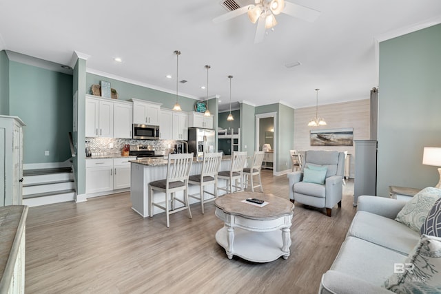 living room with ceiling fan with notable chandelier, light wood finished floors, baseboards, and crown molding