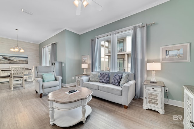 living room featuring ornamental molding, baseboards, light wood finished floors, and ceiling fan with notable chandelier